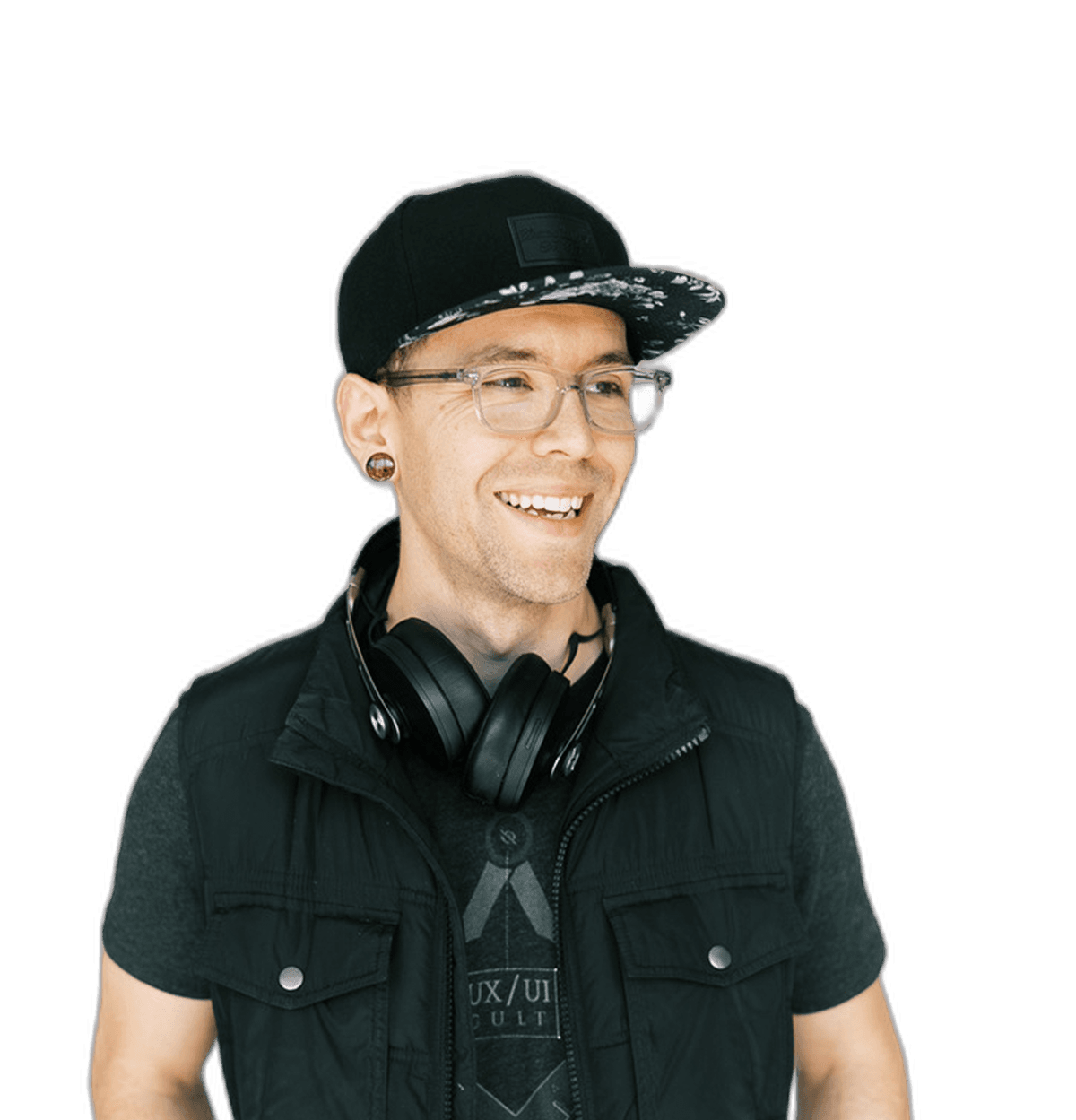 Zac Elletson — portrait, smiling, in a black snapback, clear-frame glasses, headphones around the neck, and a black vest over a UX/UI Cult tee